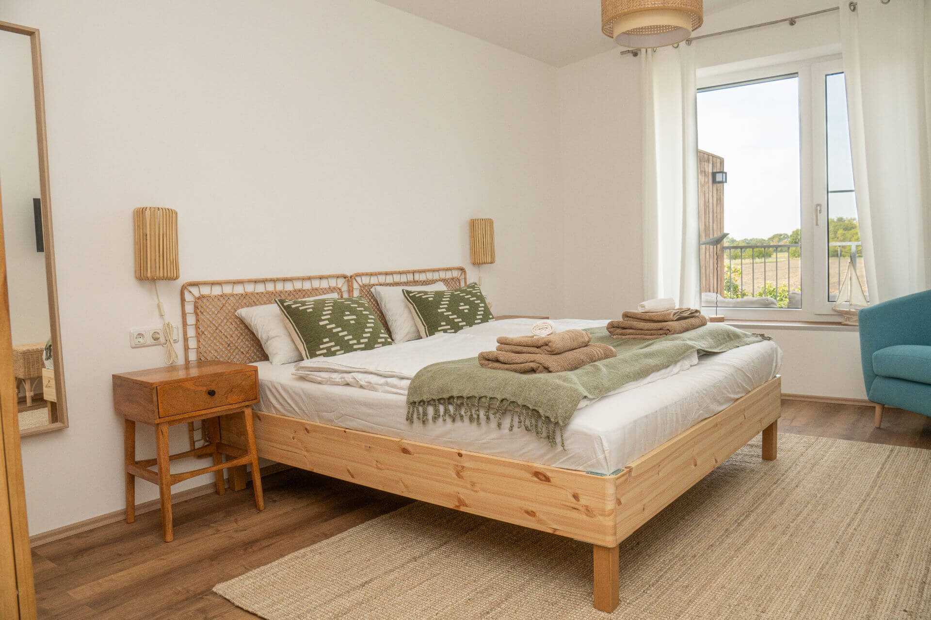 Schlafzimmer mit Holzbett, Rattan-Kopfteil und Blick ins Grüne