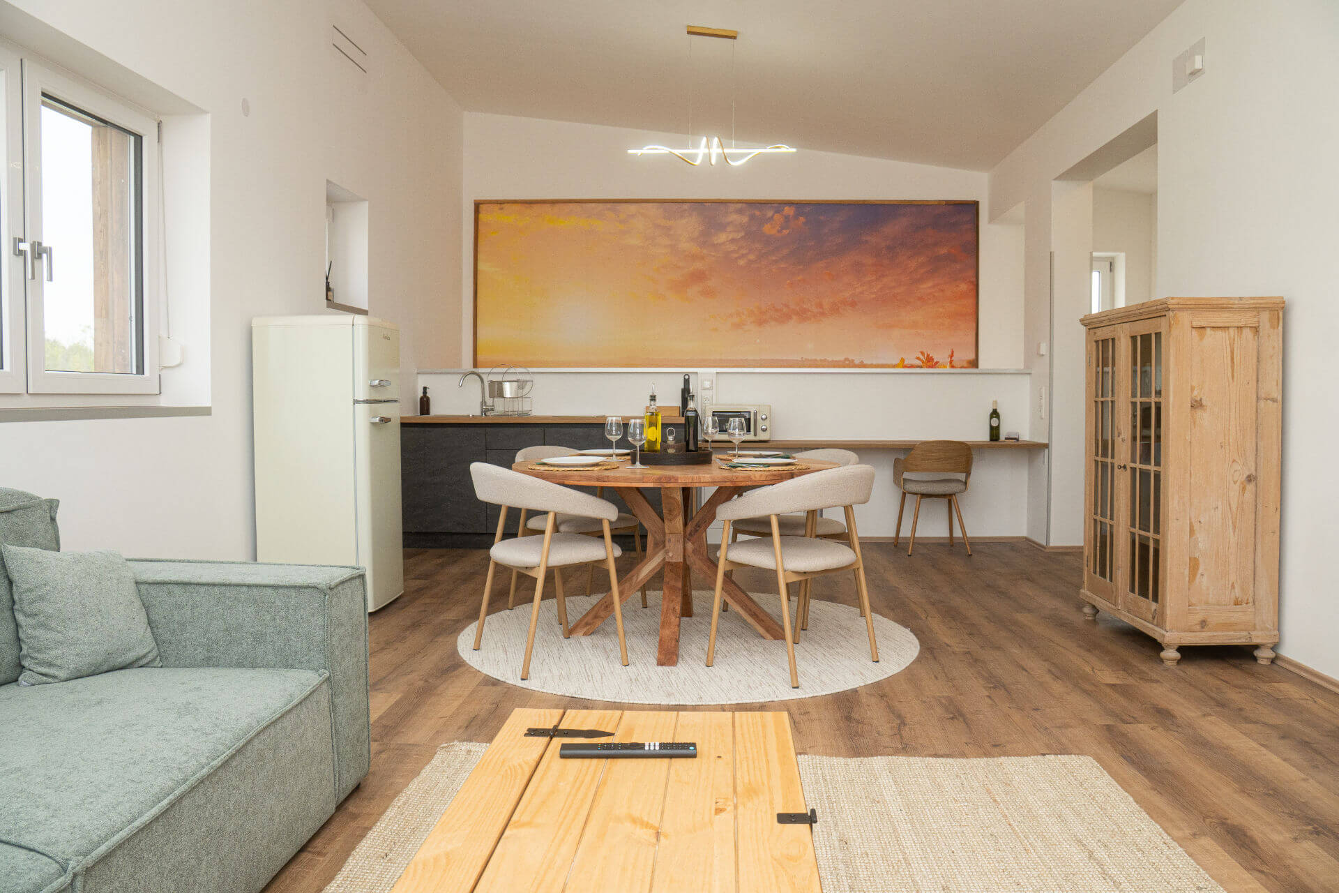 Offener Wohnraum mit Sofa, Küche und großem Sonnenuntergangs-Bild